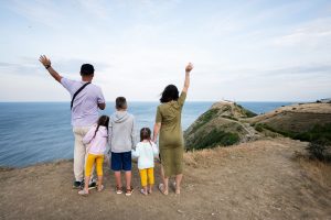 Happy family of five tanding on top of a mountain and looking at